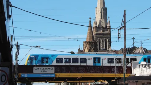 Train crosses rail bridge over Glenferrie Road with church spire in background