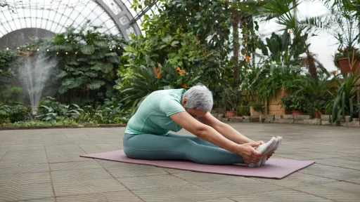 A woman has her legs out straight and is leaning forward to touch her toes.