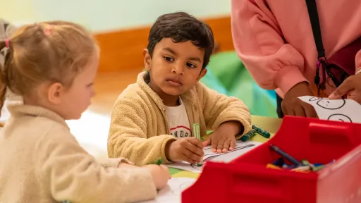 Two young children sitting at a table colouring in activity sheets with crayons