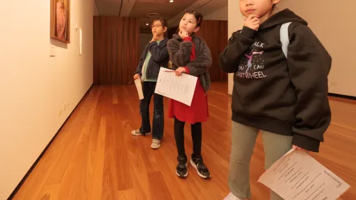 Three young people looking thoughtfully at artworks in a gallery. 
