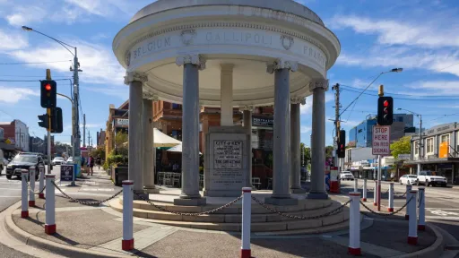 Street view of a cenotaph building on the edge of a roundabout with a historic building in background