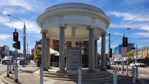 Street view of a cenotaph building on the edge of a roundabout with a historic building in background