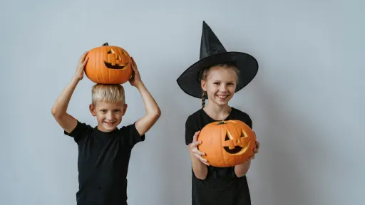 Two children wearing black are holding halloween pumpkins.