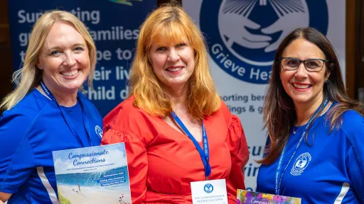 Three women standing together at an event holding brochures