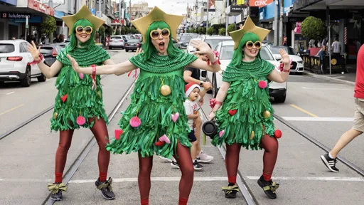 Three people stand in the middle of a busy street dressed as Christmas trees.