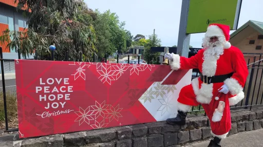 Santa standing with a banner that says 'love, peace, hope, joy, Christmas'