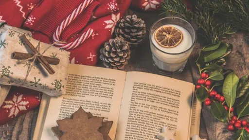 An open book is surrounded by christmas holly, candy canes, a red jumper and a wrapped present.