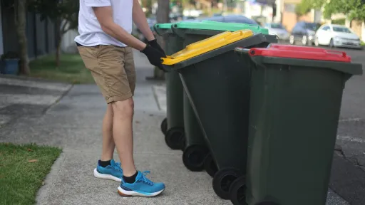 A man putting a recycling bin out on the kerb next to other bins