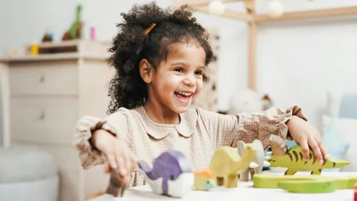 A young child sits at a table playing with toy dinosaurs.