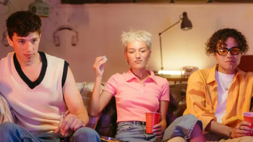 Three people are sitting on a couch holding drinks in their hands.