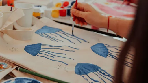 A person holding a paintbrush is painting blue jellyfish onto canvas