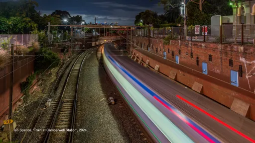 Overlooking train tracks, a train station and a train moving quickly.