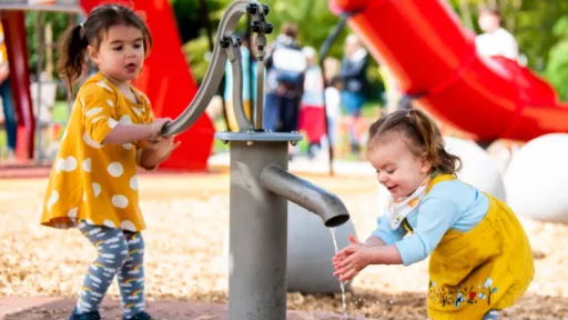 Two small girls play with water pump in playground