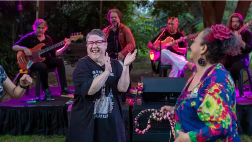 Group of people dance in front of musicians on stage in park