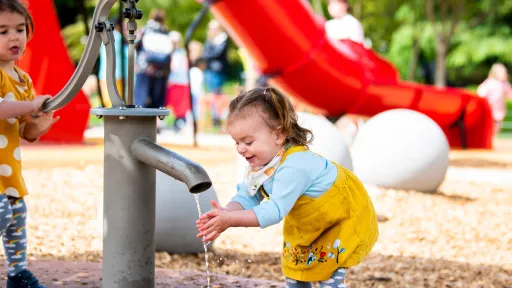 Two young girls play with water pump on playground