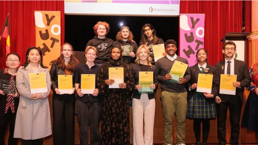 Group of young people stand in front of stage holding award certificates