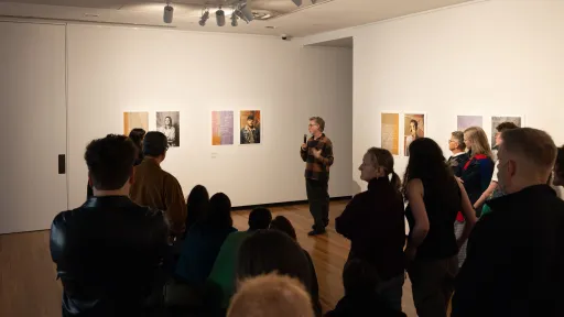 A crowded room of people on an exhibition tour with an artist speaking about their work.