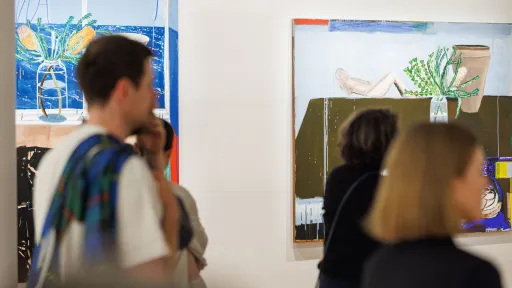 Visitors standing in front of two semi-abstract still life paintings at an exhibition tour. 