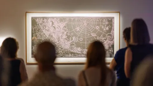 A group of people looking at an artworkwork in a dimly lit room. 