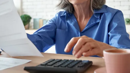 A women sitting at a table holding paper bills using a calculator