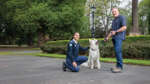 Woman in blue uniform next to white dog and its owner in park