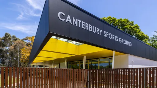Black, yellow and white sports pavilion behind fence in park
