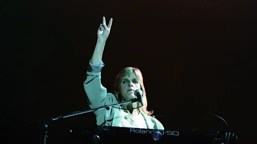 A person sitting in front of a keyboard and microphone has one hand pointing upwards