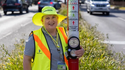 School crossing supervisor standing in median strip of road holding onto a traffic pole