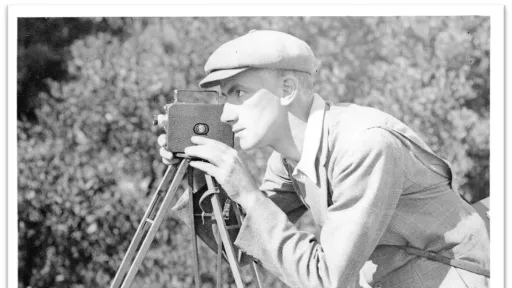 Black and white image of a man looking through an older style camera