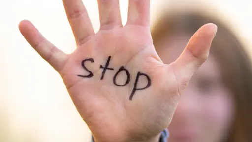 person with their hand reaching out showing their palm with the word 'stop' written on it.