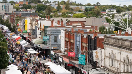 Looking down on a busy Glenferrie Road. People are everywhere for the Glenferrie Road Festival, moving between stalls and entertainment. A ferris wheel can be seen down a laneway.