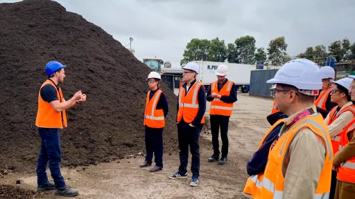 People wearing hi-vis vests and hard hats stand at a landfill site