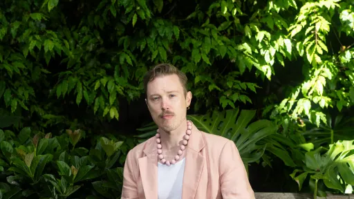 A person is sitting in front of a tree wearing a pink suit. They have a dog standing next to them