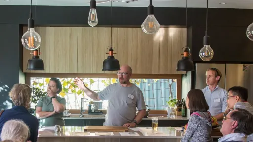 A group of people in a kitchen listening to someone speaking