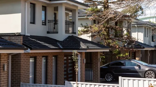 A row of brick and rendered townhouses. Each has a low fence separating the front yards.