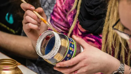 A glass jar is being held by a person who is decorating it with a paint brush