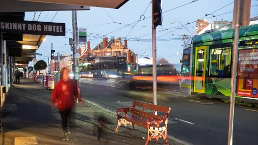 Kew Junction streetscape with person walking dog and green and yellow tram passing by
