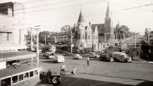 Black and white image of a Camberwell road intersection featuring old style cars, tram and buildings