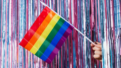 A rainbow flag is being held in front of a background of purple and pink streamers