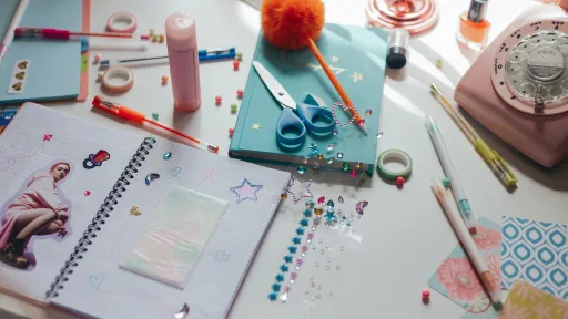 A variety of craft items are sitting on a table. There is a notebook, scissors, glue, pencils and stickers.