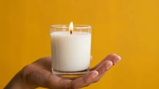 A candle is sitting in the palm of a hand against an orange background.