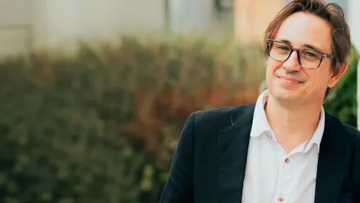 A person wearing glasses and short brown hair is smiling at the camera