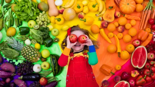 Young child is surrounded by rainbow of fruit and vegetables