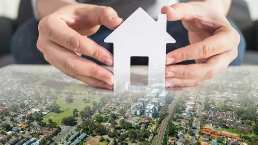 Two hands holding a white cut out house shape over a suburban landscape.