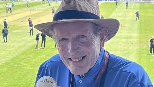 A person wearing a hat and blue shirt is holding a cricket ball