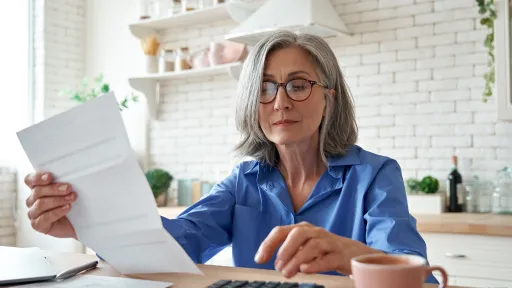 Woman at a table looking at a bill with her calculator nearby