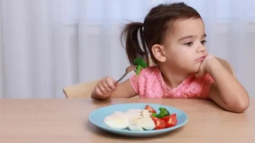 a child sits at a table and ignores the plate of food in front of her