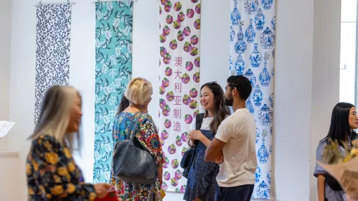 visitors to an art exhibition stand in front of colourful, vertical artworks on a white wall
