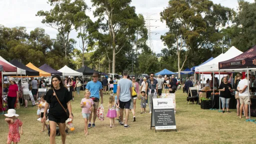 market stalls line both sides. Families walk between stalls looking at and buying products. In the background are the tall gum trees of Patterson Reserve.