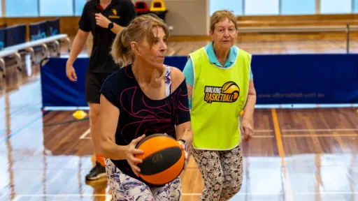 Player holds basketball on indoor basketball court with another player and referee in background